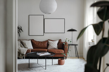 Blank vertical and horizontal din A posters with black frames in light room interior design. Frame mockups on a white wall, scandinavian living room, brown leather sofa, coffee table, potted plants