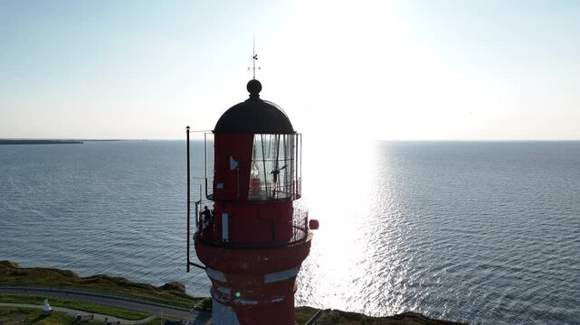 Red and White Lighthouse on Pakri Cliff, Estonia. A red and white lighthouse stands tall on Pakri Cliff, overlooking the blue sea and surrounded by green vegetation.