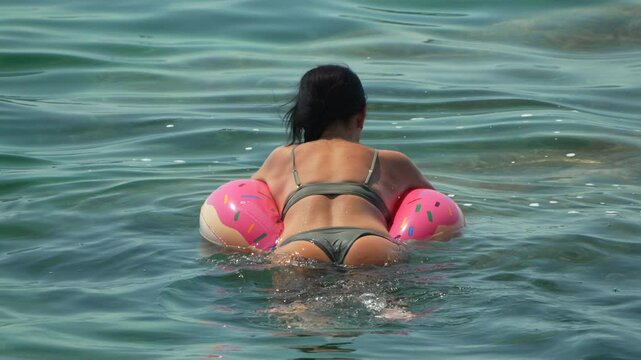 Woman Swimming Inflatable Floats Ocean on a pink donut-shaped inflatable