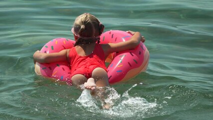 Girl Donut Float Summer - A young girl wearing a red swimsuit and a snorkel mask enjoys a sunny day floating on a pink donut-shaped inflatable in the clear blue water.