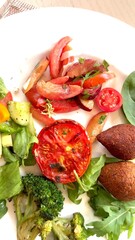 Greens , tomato, broccoli salad with plums on white plate offering nutritious lunch option at restaurant Fresh healthy ingredients are skillfully presented making Flavorful meal in gourmet setting.