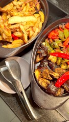 Hotel display of baked eggplants, pepper, zucchini, and potato in cast iron plates. Warm and inviting presentation that emphasizes wholesome, roasted goodness of these vegetables.
