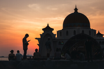 Naklejka premium Silhouettes looking out to a mosque in the sea