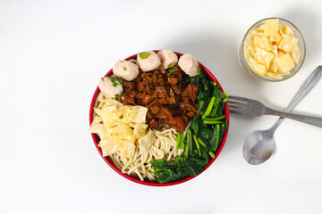 A bowl of Mie Ayam, a typical Indonesian dish, featuring chicken noodles with shredded chicken, meatballs, dumplings, green vegetables, and a variety of toppings, isolated on a white background