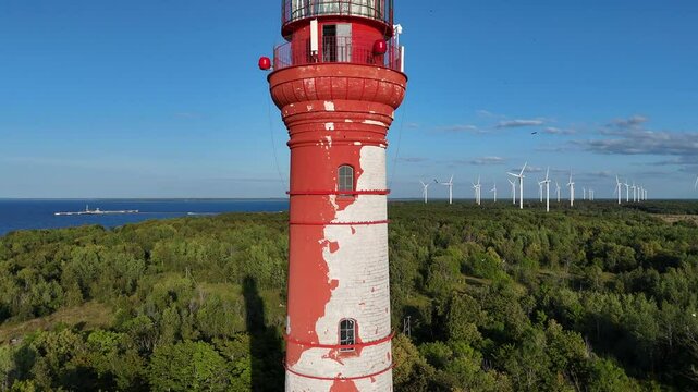 Red and White Lighthouse on Pakri Cliff, Estonia. A red and white lighthouse stands tall on Pakri Cliff, overlooking the blue sea and surrounded by green vegetation.