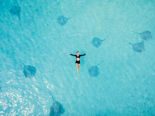 Woman swims in sea with stingrays in Maldives. Stingray fishes and floating woman in blue ocean. Drone view