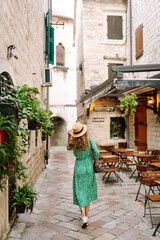 A young woman wearing a green floral dress and a wide-brimmed hat strolls through a picturesque...
