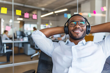 Obraz premium Relaxed young professional enjoying music with headphones in a contemporary office, hands behind his head, surrounded by colorful sticky notes.