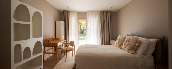 Panoramic view of a master bedroom, with modern bookshelves and a desk with a bamboo chair. The curtains are drawn, but the greenery of the garden can be seen from the window. No one inside © alexandre zveiger