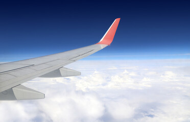 Fototapeta premium View from inside of plane through porthole. Wing of airplane at cloudscape. View from an aircraft window. Plane's wing with white clouds and blue sky