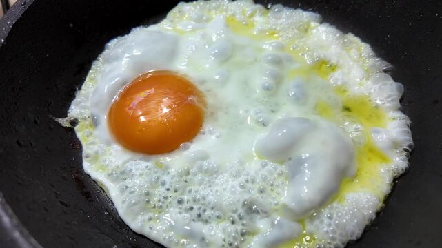 Primer plano de un huevo fri&eacute;ndose en una sart&eacute;n caliente con aceite, video culinario de cocina casera y desayuno tradicional, gastronom&iacute;a, alimentaci&oacute;n y preparaci&oacute;n de alimentos