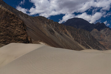 View of sand dunes in the foreground and High-altitude Mountain ranges in the background in Nubra valley, Ladakh India. 