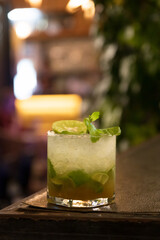 Refreshing mojito cocktail featuring mint leaves, lime, and ice, set against a blurred background for a vibrant nightlife atmosphere.