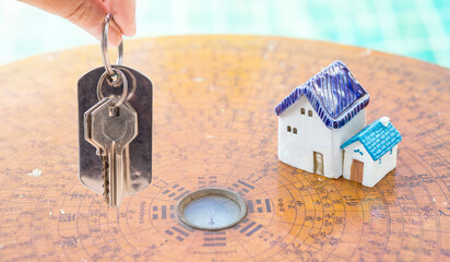 House key in girl hand with miniature house on ancient wooden Chinese compass, property and real...
