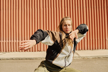 Woman with light hair practicing dance moves in front of urban wall resembling ribs pattern creating dynamic pose and captivating energy