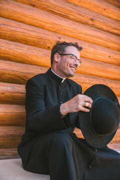 Joyful priest laughing while holding his hat outdoors