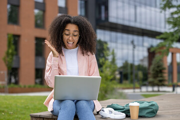 African American student experiences excitement while working on laptop outdoors on college campus. Young adult studies with enthusiasm in modern educational setting, showcasing technology, learning