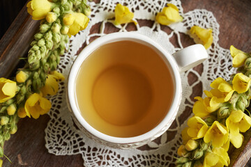 A white cup of herbal tea with fresh blooming mullein or Verbascum densiflorum plant