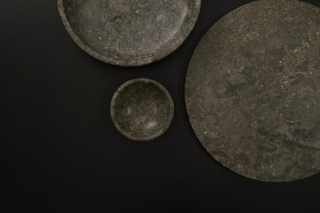 Top view of brown marble tray, plate and bowl on black background. Food presentation, dishes, stone tray. Copy space, flat lay.