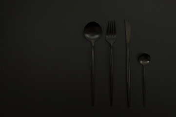 Top view of black cutlery on black background. Knife, fork, spoon and dessert spoon. Copy space,...