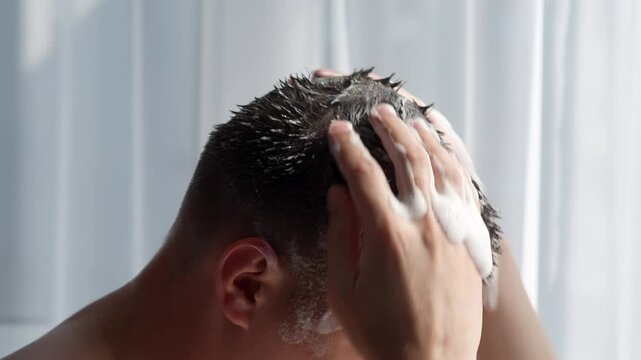 A young guy of European appearance washes his hair with shampoo in the shower.
A man takes a shower.
Healthy scalp.
Body care.
Personal hygiene