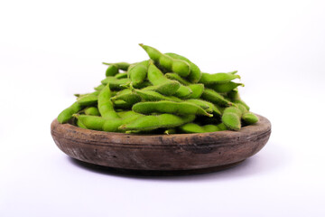 Fresh edamame beans are placed in a rustic wooden bowl, with ample copy space, isolated on a white background