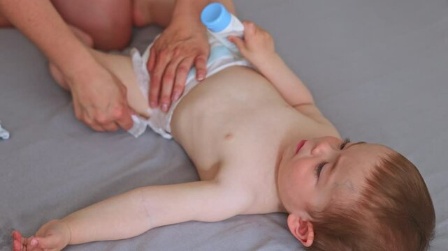 portrait of cute baby boy lying on bed.mother changing kids diapers, infant moving legs.blonde caucasian child is smiling, close up of head.motherhood period, stay home 