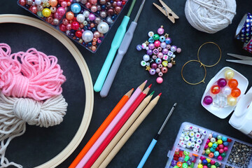 Colorful beads, coloring pencils, glitter, needles, string, hoop, tape and scissors on dark...