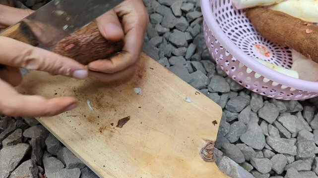 peel skin,and slice raw cassava (tapioca) root using knife in a wood cutting board, cooking, preparation,4K.