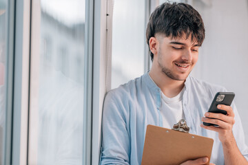 Fototapeta premium young man with mobile phone and documents next to the window