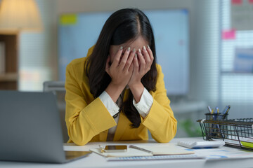 Stressed Asian businesswoman having headache in office with laptop financial business online...