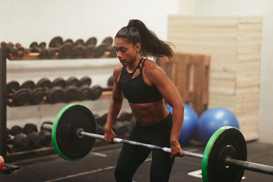 Muscular young indian woman lifting weights during a gym class. She is wearing a top and her hair is in a tight ponytail