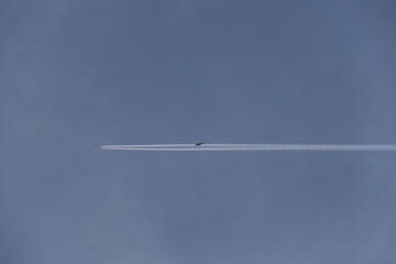 White contrails behind an airplane in a bright, cloudless sky