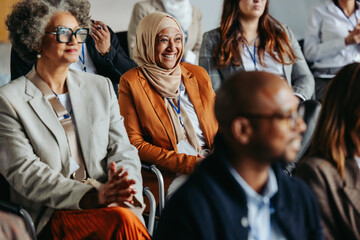 Diverse group of professionals attending a business conference with a Muslim woman smiling in the audience - Powered by Adobe