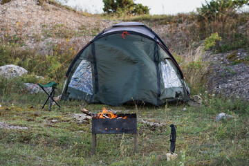 Wild camping in nature, tent, burning barbecue and survival knife.