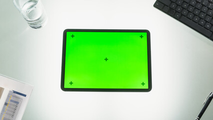 Top View of a Tablet Computer with Mock Up Green Screen Chromakey Display with Motion Trackers Standing on an Office Desk Next to Keyboard, Black Pen, Documents and a Glass of Water