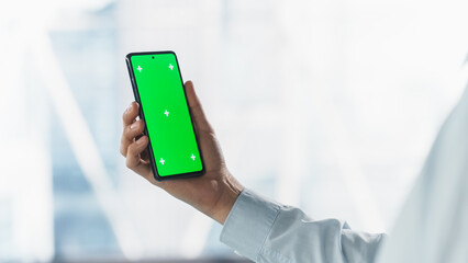 Anonymous Businessman Holding Smartphone with Green Screen Mock Up Display, Standing in a Modern Office. Photo Template for Digital Presentations, Business Content Creation, Corporate Communication
