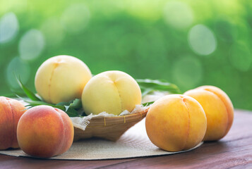 Fresh three kinds of peaches on blurred greenery background, Three colored peaches in basket on wooden table in garden.