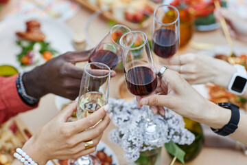 Close-up of friends toasting drinks at festive table setting during holiday season, showing diverse hands and glasses, surrounded by food and drink