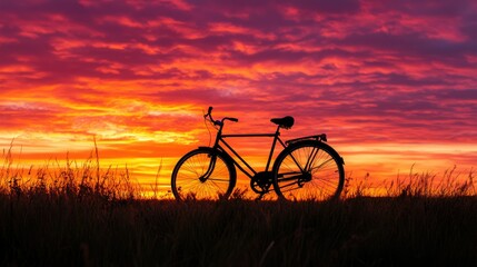Obraz premium A bicycle silhouetted against a stunning sunset landscape, with the sky ablaze in warm colors and the horizon stretching into the distance.