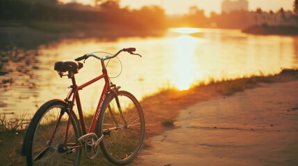 Obraz premium An old bicycle stands on a riverside path, bathed in warm sunset light, evoking a nostalgic and tranquil mood.