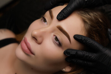 Photo of a girl after the procedure of permanent makeup, the master demonstrates the girl's eyebrow after the completion of tattooing. Permanent eyebrow makeup, eyebrow tattooing with brown pigment