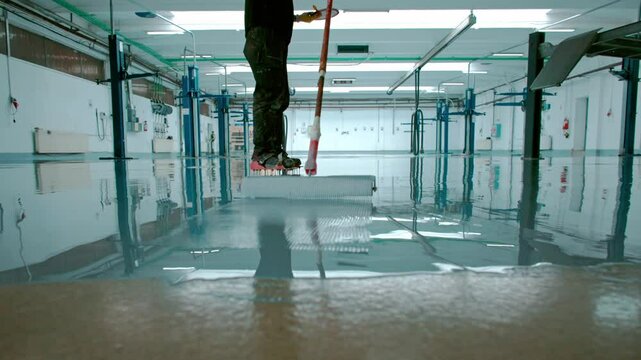 Epoxy floor Construction worker is applying epoxy resin on a large surface in slow motion