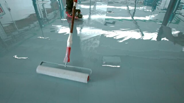 Epoxy floor Construction worker applies a layer of epoxy resin to a floor to create a smooth and durable surface
