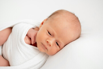 a newborn baby is lying in a diaper on a bed on a white isolated background, a place for text, a small baby boy is sleeping sweetly, a close-up portrait
