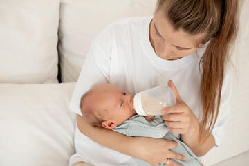 feeding a baby from a bottle, a mother feeds a newborn baby with milk while holding it in her arms, baby food, a baby sucks a bottle