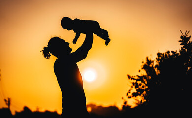 Silhouette of a breathtaking sunset. A father joyfully lifts his child into the air, celebrating a...
