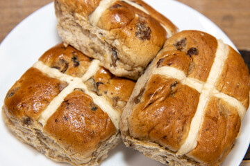 A delicious plate of three hot cross buns on a kitchen table