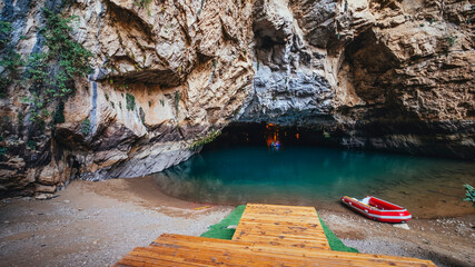 A photo of the magnificent cave entrance and a boat waiting for those who want to visit the Altinbesik cave by boat. Antalya, Turkey.