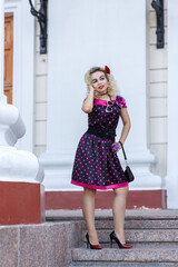 Blonde girl in a bright dress and sunglasses on the street near a building on a walk on a summer...
